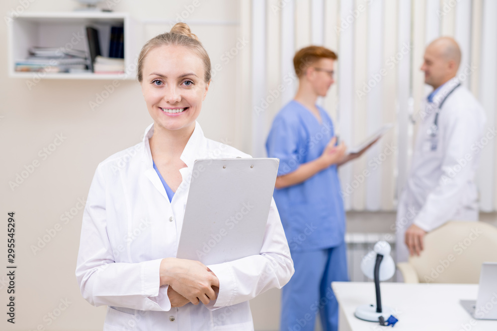 Young cheerful doctor in whitecoat holding clipboard with document Young cheerful doctor in whitecoat holding clipboard with document