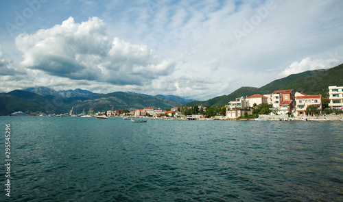 Bay in seaside town with boats, houses in green mountains on blue sky,.Tivat, Montenegro