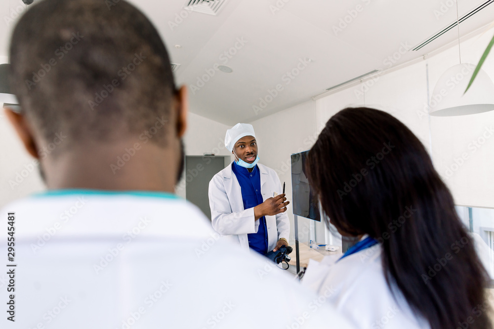 Obraz premium Doctors team with x-ray. Health care. Radiology. Team Of Experts Doctors Examining X-ray Report In Hospital. African man doctor standing near the board