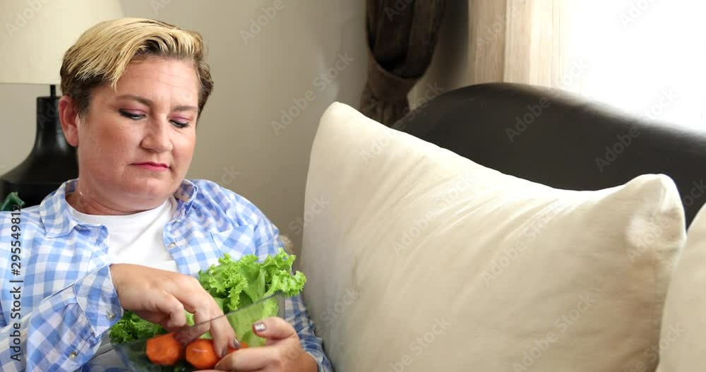 Portrait of a caucasian middle aged woman sitting on sofa and eating low calorie food. Diet. Dieting concept. Healthy Food. Portrait of a caucasian middle aged woman sitting on sofa and eating low calorie food. Diet. Dieting concept. Healthy Food.