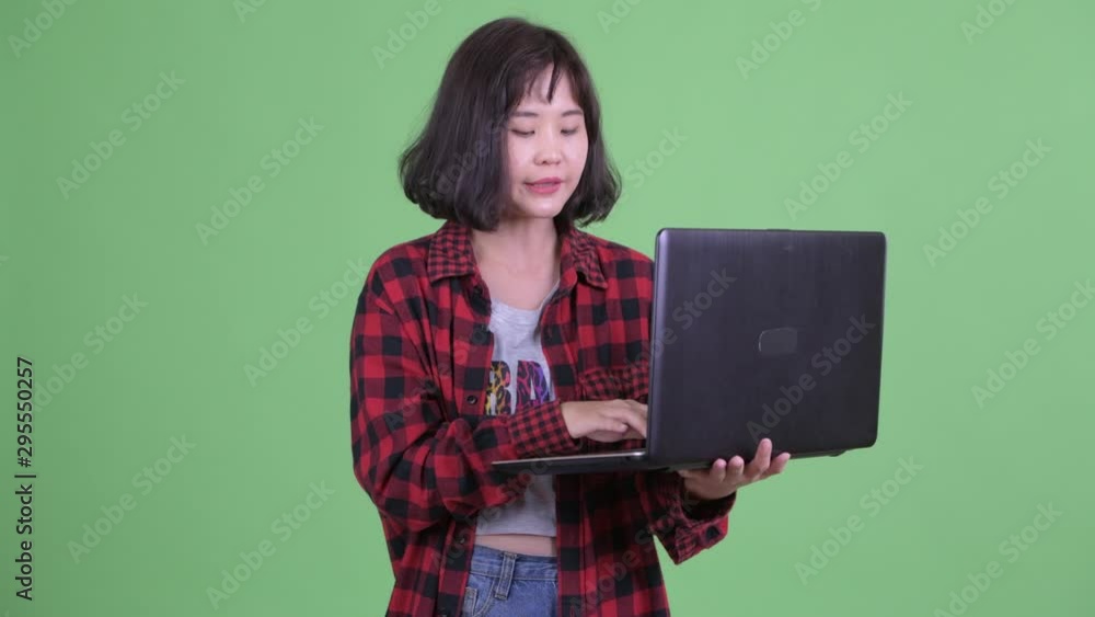 Happy Asian hipster woman talking while using laptop Happy Asian hipster woman talking while using laptop