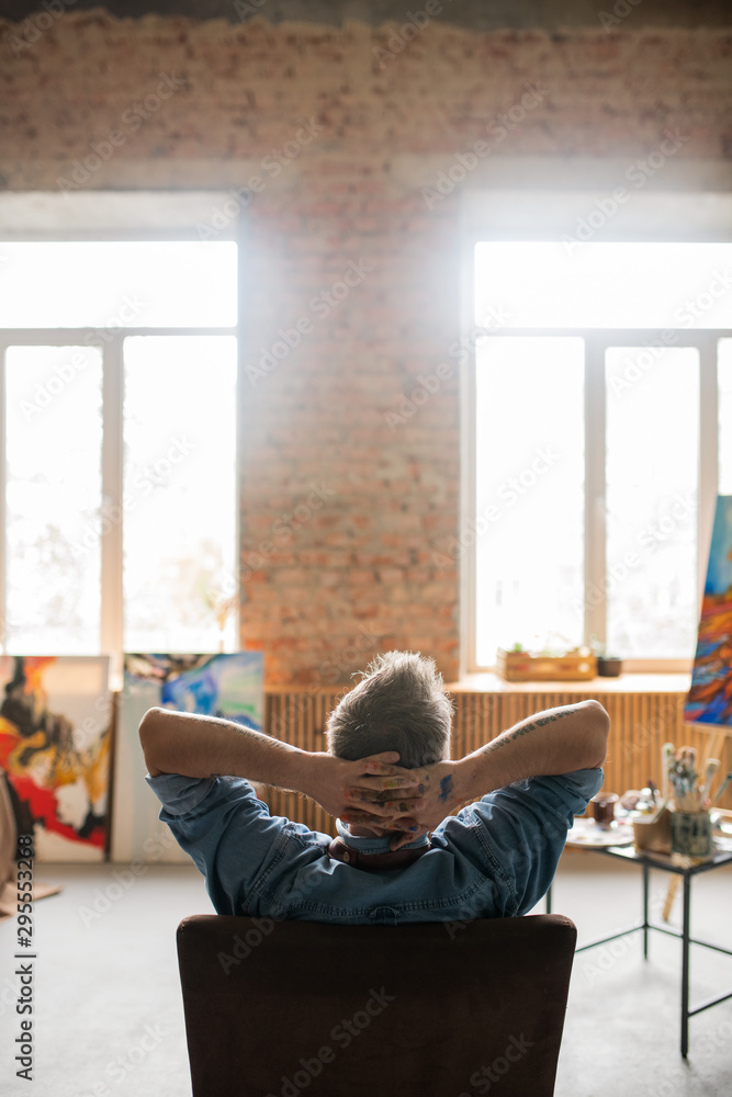 Back view of contemporary restful artist keeping his hands behind head Back view of contemporary restful artist keeping his hands behind head