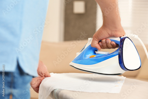 Handsome man ironing clean laundry at home, closeup