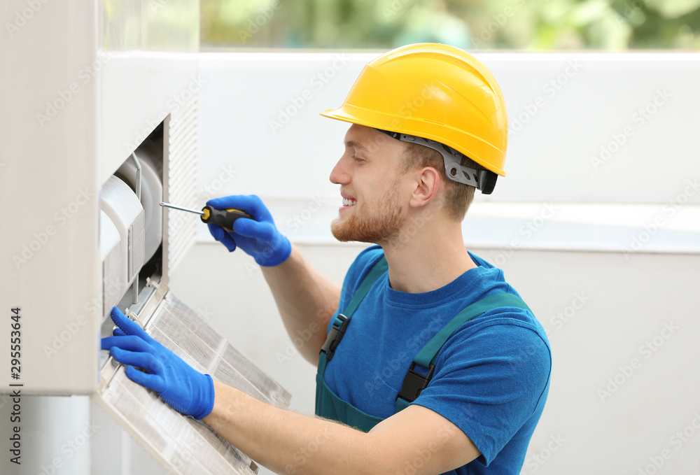 Professional technician maintaining modern air conditioner indoors Professional technician maintaining modern air conditioner indoors