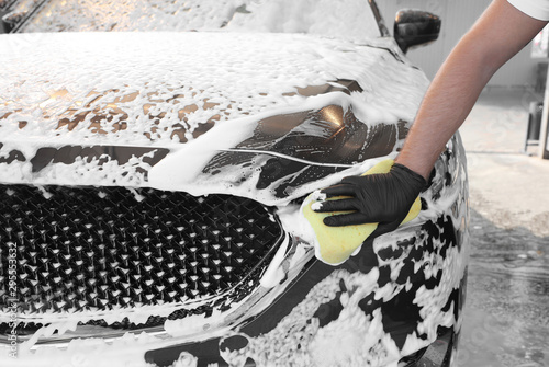 Young worker cleaning automobile with sponge at car wash, closeup