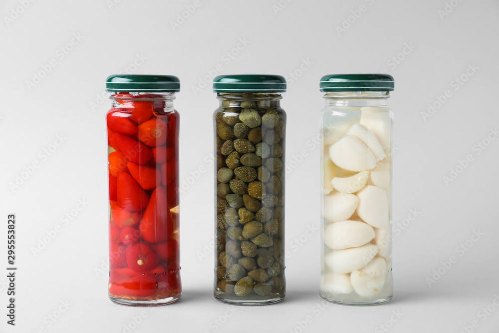 Jars of pickled red hot piri-piri peppers, capers and garlic on light grey background Jars of pickled red hot piri-piri peppers, capers and garlic on light grey background