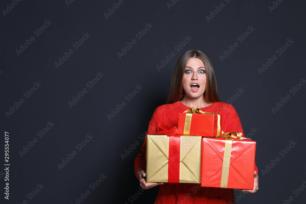 Emotional young woman with Christmas gifts on dark background. Space for text Emotional young woman with Christmas gifts on dark background. Space for text