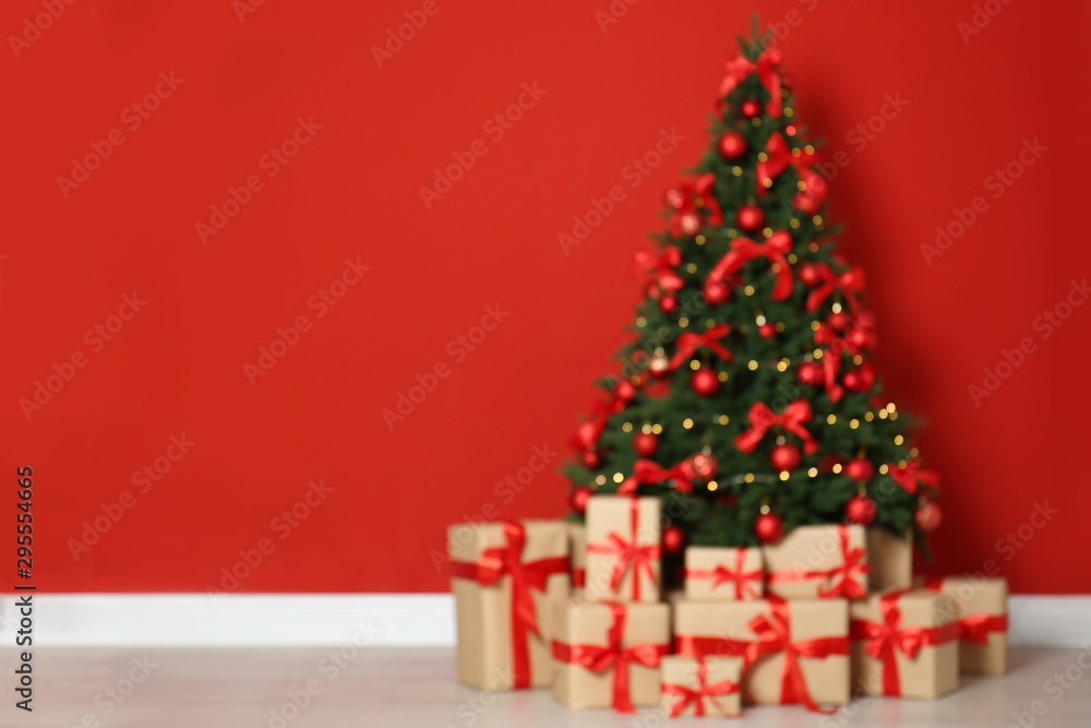 Blurred view of decorated Christmas tree and gift boxes near red wall. Space for text