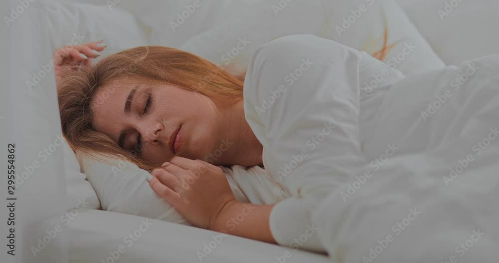 Beautiful young woman is sleeping soundly in bed in the bedroom. Cozy room with white pillows and a blanket. Portrait view. Beautiful young woman is sleeping soundly in bed in the bedroom. Cozy room with white pillows and a blanket. Portrait view.