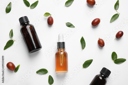 Glass bottles with jojoba oil and seeds on white background, top view photo