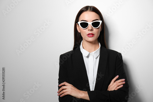 Young businesswoman in stylish sunglasses on light background, space for text