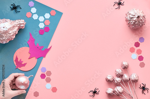 Creative paper craft Halloween flat lay on pink and grez split paper background with copzßspace. Hand holding pink painted pumpkin,  bats with Moon, black spiders and hexagons. photo