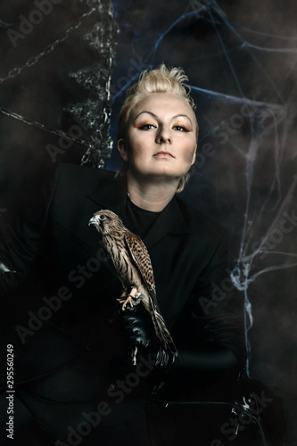 Photo of a female witch queen holding bird and sitting on a gothic scary black throne
