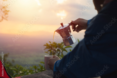 Male tourists pouring coffee from moka pot, men with coffee and beautiful natural background, tents, mountain peaks photo