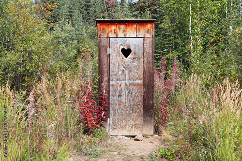 An outhouse in a wooded area with a heart window photo