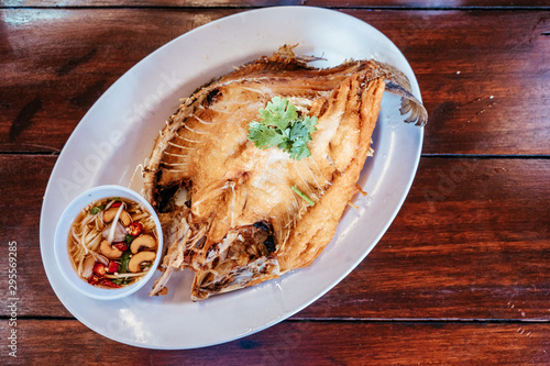 Deep fried Snapper topped with fish sauce in white dish serving on table. Pla kapong tod num pla. Popular traditional Thai style food. photo