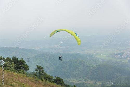 a yellow paraglider flying over the mountains