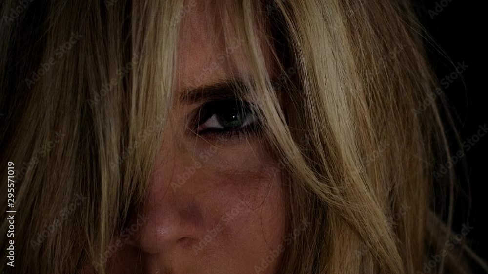 Young blond woman looks intensely at camera; close up; dramatic low key light. Young blond woman looks intensely at camera; close up; dramatic low key light.