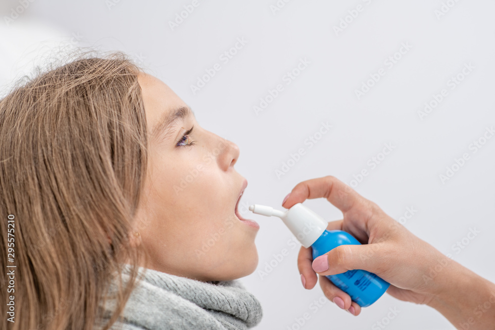 Mother using medical spray for young girl at home. Side view Mother using medical spray for young girl at home. Side view
