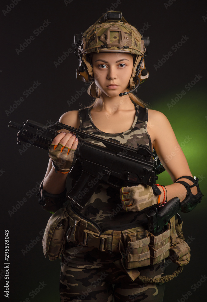 the girl in military airsoft clothes poses with a gun in her hands on a dark background the girl in military airsoft clothes poses with a gun in her hands on a dark background
