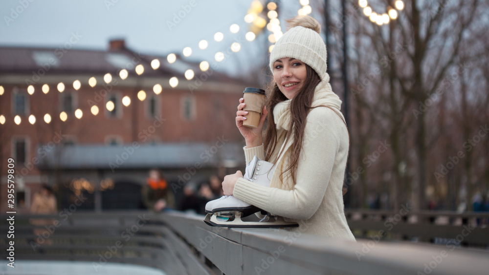 Charming young woman in the Park near the ice rink. Smiling brunette with skates - obrazy, fototapety, plakaty 