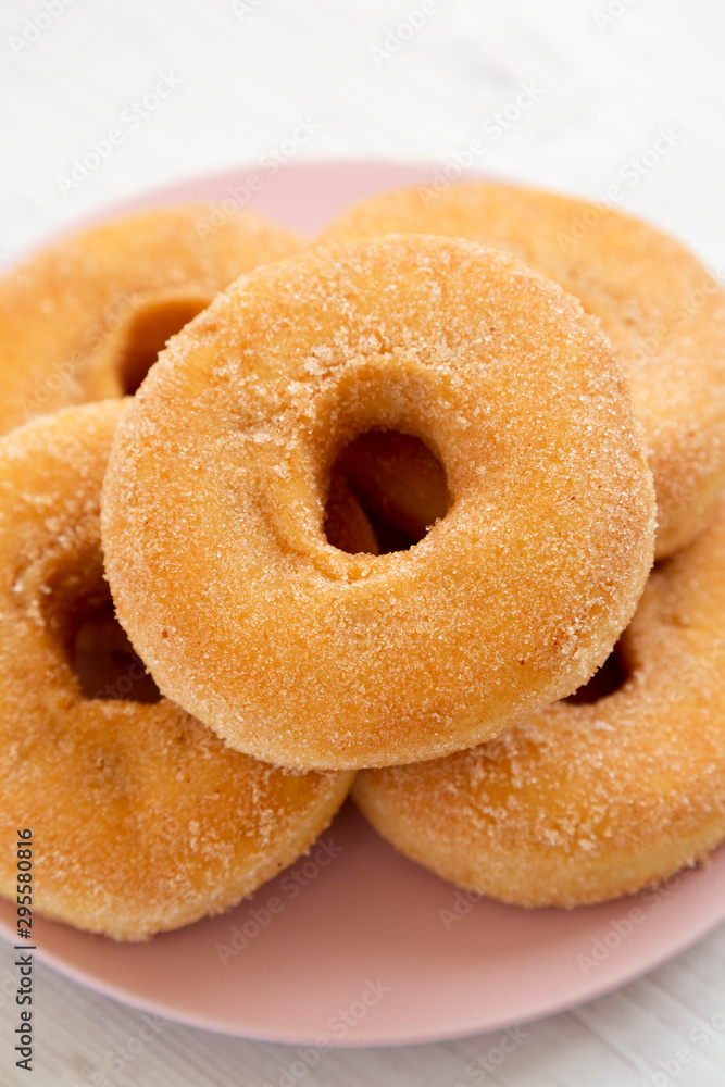 Homemade autumn apple-cinnamon donuts on a pink plate on a white wooden background, low angle view. Close-up.