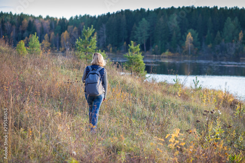 An adult woman with a backpack travels through the autumn forest, enjoying nature. © papa