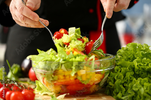 Cook holds fork in hand and mixes salad fresh vegetables seasoned with olive oil. Raw food and vegetarian in modern society is popular concept.