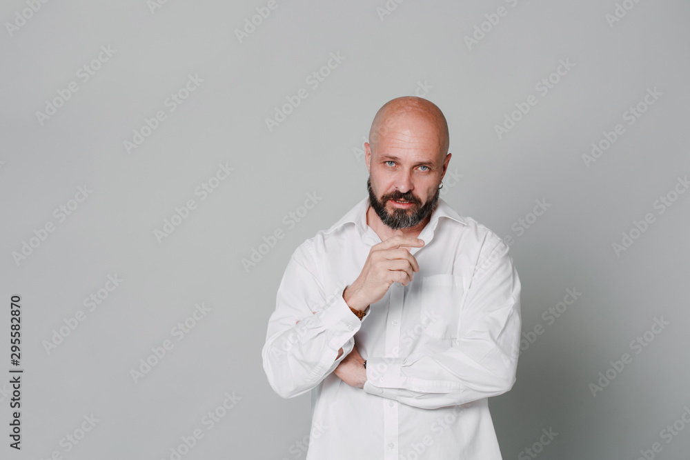 Serious middle-aged man with folded arms and a deadpan expression posing in front of a gray background with copy space Serious middle-aged man with folded arms and a deadpan expression posing in front of a gray background with copy space