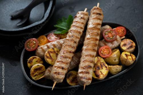 Grilled chicken kebabs with roasted potatoes and cherry tomatoes, studio shot on a black stone background