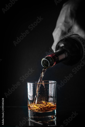  Pouring cognac or whiskey from the bottle into the glass against black background