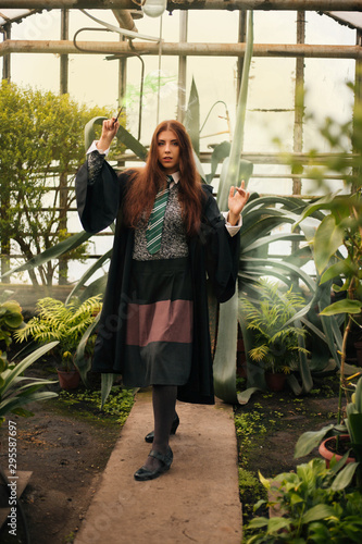 A girl from the school of young wizards with a magic wand in his hand. Green magic. A sorceress conjures among plants in a greenhouse, a botany lesson is cosplay.