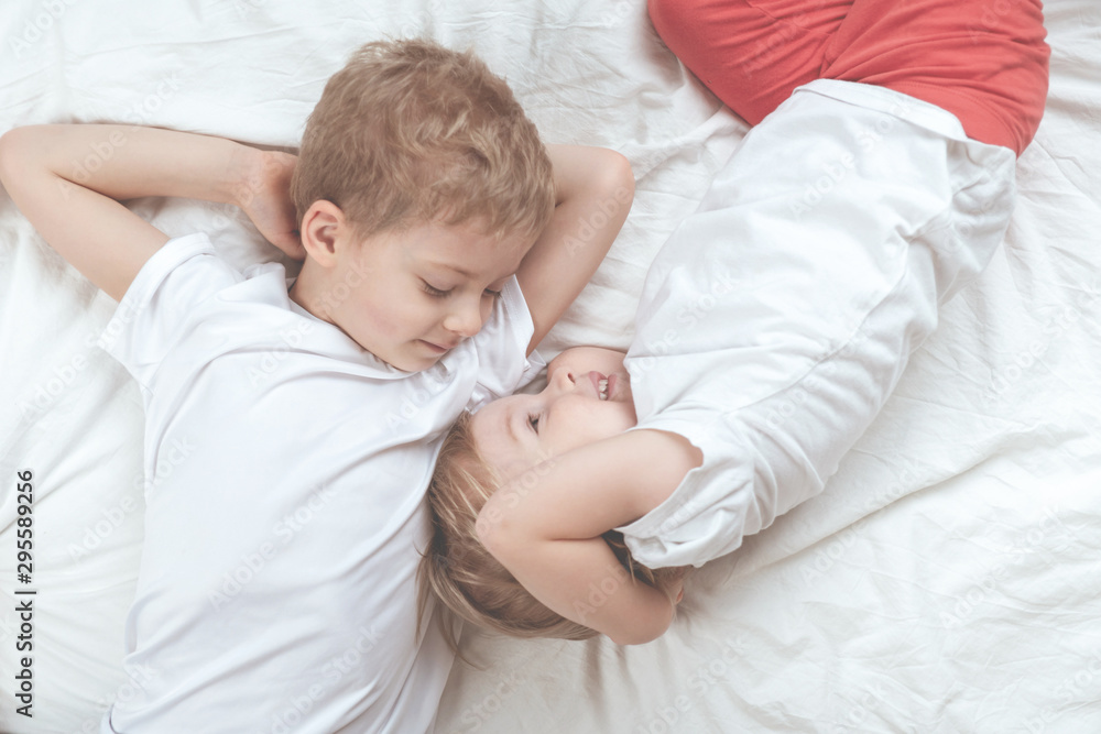 children in white t-shirts lie on the bed. brother and sister together children in white t-shirts lie on the bed. brother and sister together