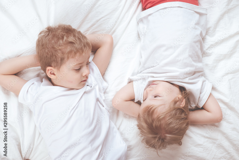 children in white t-shirts lie on the bed. brother and sister together children in white t-shirts lie on the bed. brother and sister together