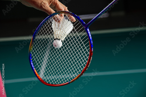Hand of Badminton player holding shuttlecock and Badminton racket ready to serve with green blurred court background. © Jack Tamrong