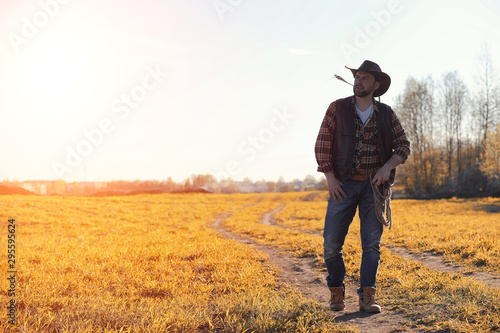 A man cowboy hat and a loso in the field. American farmer in a field wearing a jeans hat and with a loso. A man is walking across the field in a hat
