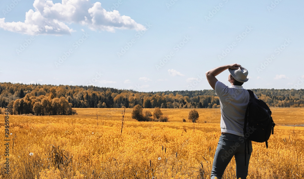A young man is traveling in nature. Traveling with a backpack on the shoulders of a beautiful park. Hitchhiking with one bag in autumn. A young man is traveling in nature. Traveling with a backpack on the shoulders of a beautiful park. Hitchhiking with one bag in autumn.