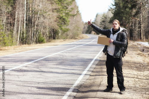 A young man is hitchhiking around the country. The man is trying to catch a passing car for traveling. The man with the backpack went hitchhiking to the south. photo