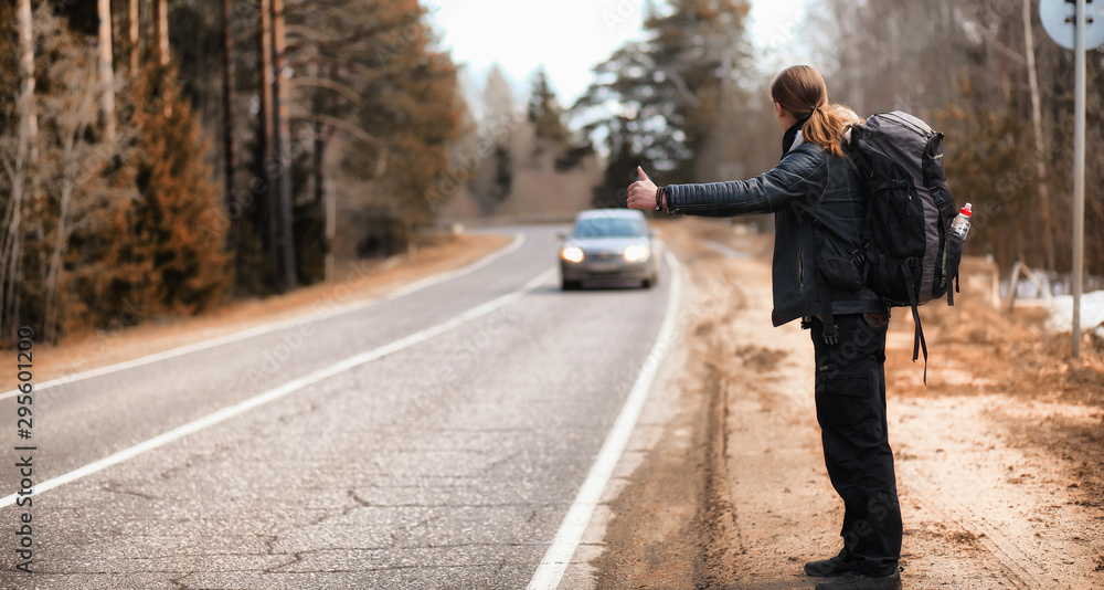 A young man is hitchhiking around the country. The man is trying to catch a passing car for traveling. The man with the backpack went hitchhiking to the south. A young man is hitchhiking around the country. The man is trying to catch a passing car for traveling. The man with the backpack went hitchhiking to the south.