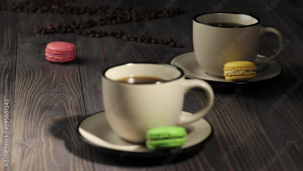 Composition from coffee beans. Wooden table background decorated with coffee beans, color macaroons and mugs with coffee. Focus moves from background to foreground. 4K Composition from coffee beans. Wooden table background decorated with coffee beans, color macaroons and mugs with coffee. Focus moves from background to foreground. 4K