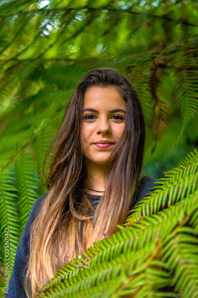 a young brunette tucked into green plants looking at camera a young brunette tucked into green plants looking at camera