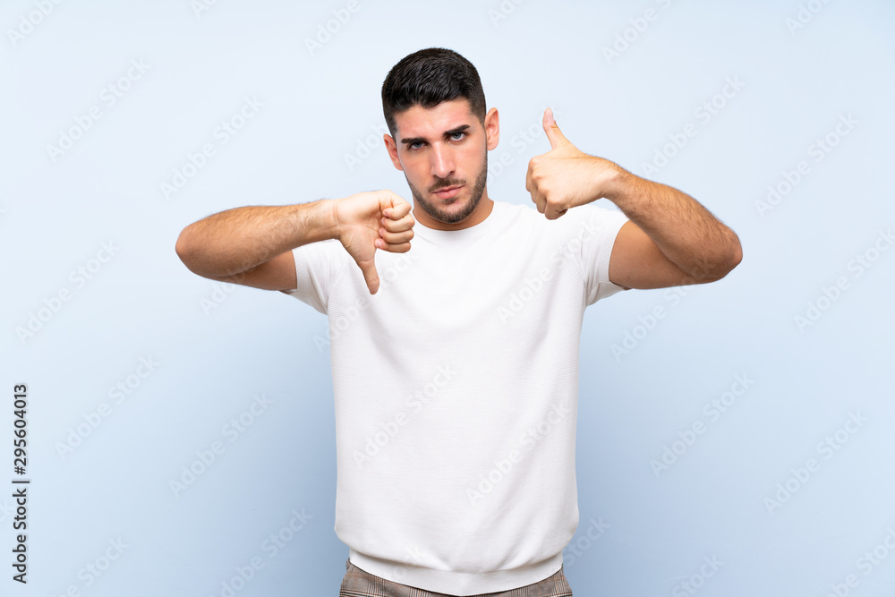 Caucasian handsome man over isolated blue background making good-bad sign. Undecided between yes or not Caucasian handsome man over isolated blue background making good-bad sign. Undecided between yes or not
