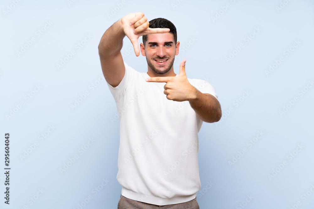 Caucasian handsome man over isolated blue background focusing face. Framing symbol Caucasian handsome man over isolated blue background focusing face. Framing symbol
