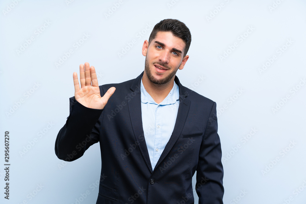 Handsome man over isolated blue background saluting with hand with happy expression Handsome man over isolated blue background saluting with hand with happy expression