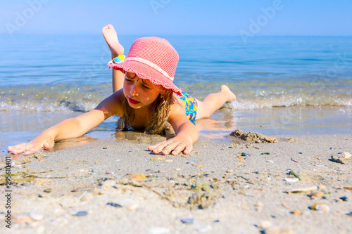 Fototapeta Child girl with summer hat is lying on the stomach in shallow sea water