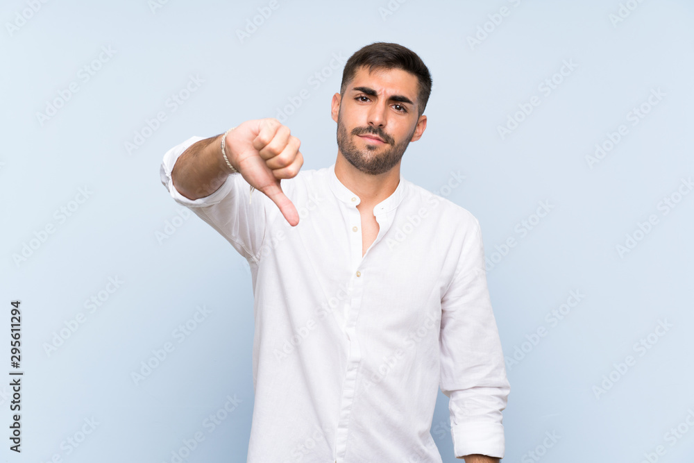 Handsome man with beard over isolated blue background showing thumb down with negative expression Handsome man with beard over isolated blue background showing thumb down with negative expression