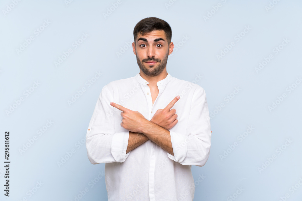 Handsome man with beard over isolated blue background pointing to the laterals having doubts Handsome man with beard over isolated blue background pointing to the laterals having doubts