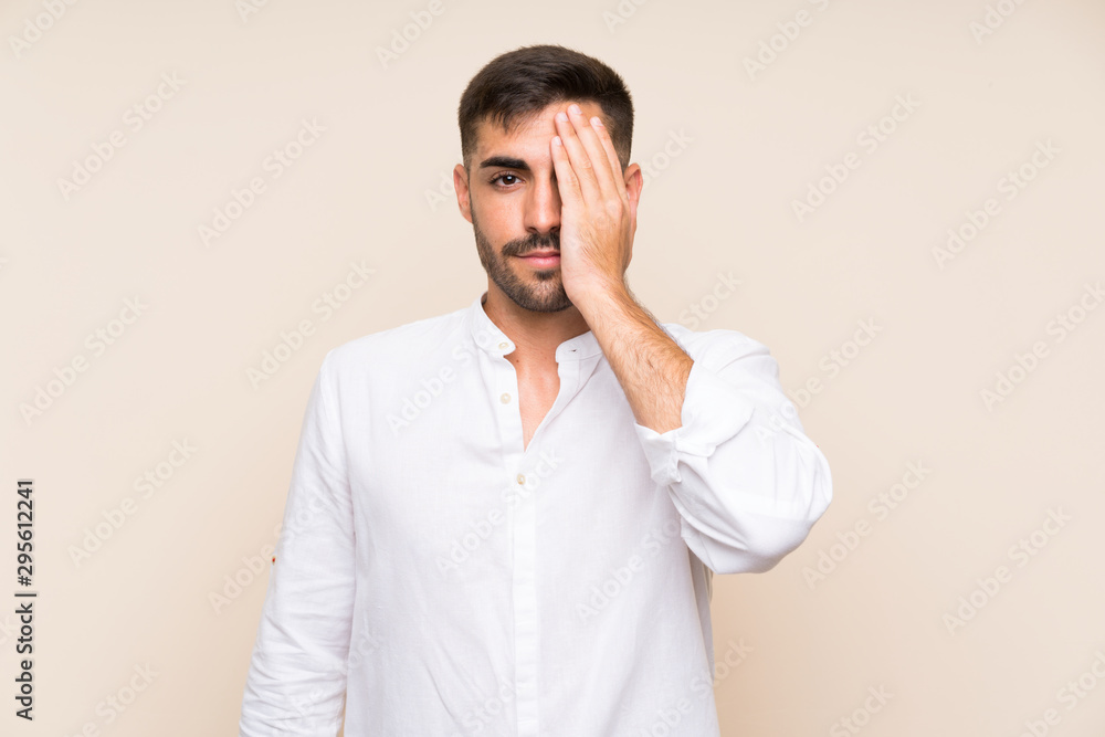 Handsome man with beard over isolated background covering a eye by hand Handsome man with beard over isolated background covering a eye by hand