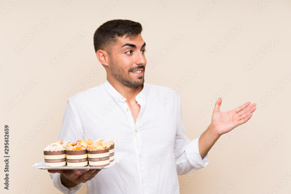 Handsome man holding muffin cake over isolated background with surprise facial expression Handsome man holding muffin cake over isolated background with surprise facial expression