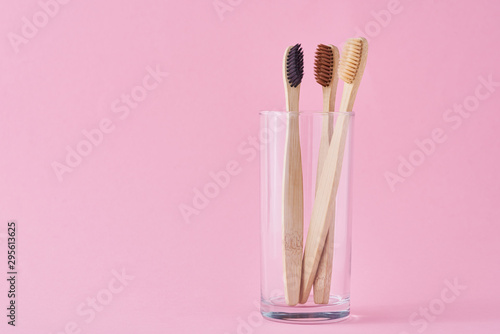 Three wooden bamboo toothbrushes in glass on a pink background. Dental care hygiene concept